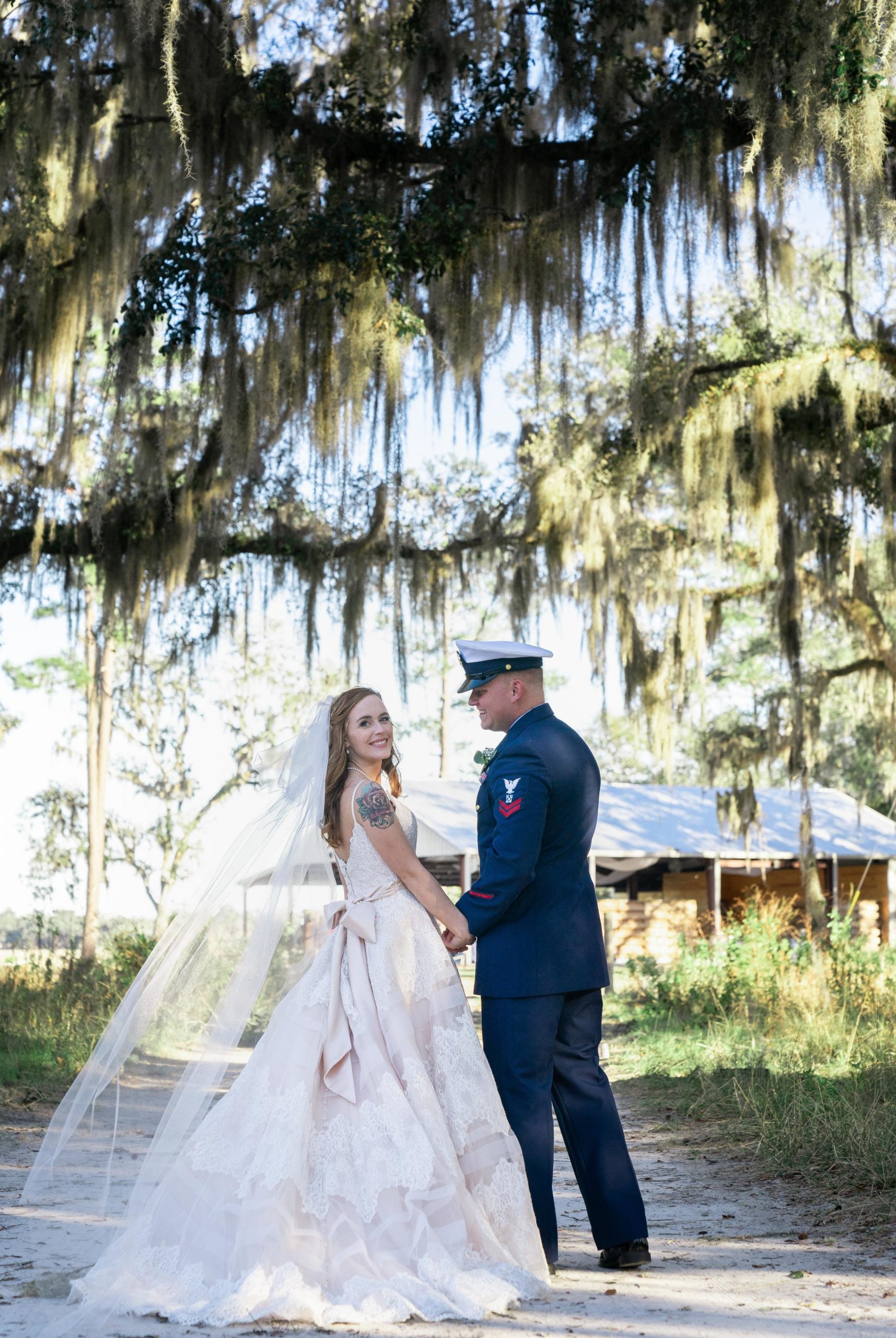 wedding portrait of couple walking with bride looking back on a dirt road under spanish moss oak trees in kingsland georgia at the bluff venue