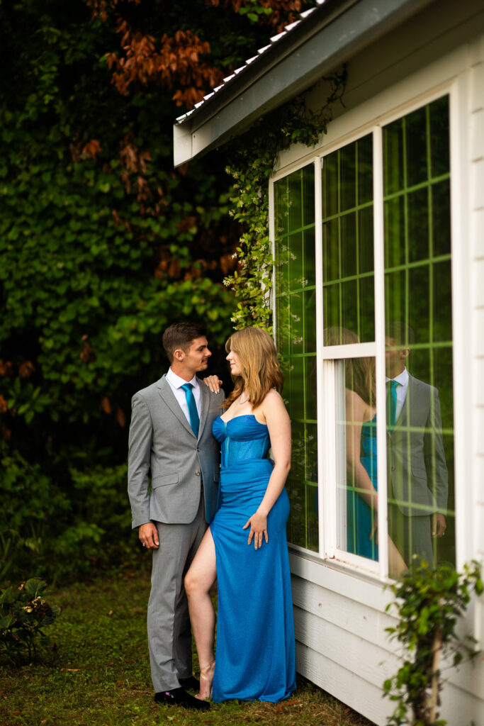 Prom pictures in front on greenery and a white cottage looking at each other